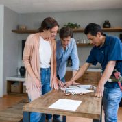 Happy Latin American plumber fixing a pipe and talking to his clients in the kitchen - domestic life concepts