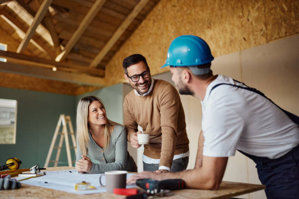 Happy couple talking to manual worker about housing plans at construction site